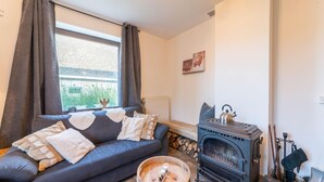 A cozy living room with a dark blue sofa, a wooden coffee table, and a wood-burning stove. - Farmhouse Kalys in Vielsalm With 180° View of the Forest (Vielsalm)
