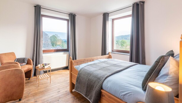 A bedroom with a wooden bed, a chair, a small table, and a lamp. - Farmhouse Kalys in Vielsalm With 180° View of the Forest (Vielsalm)