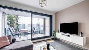 A modern living room with a sofa, a glass coffee table, a TV, and a balcony with chairs. - Cosy Apartment in Oostende With Private Terrace (Ostend)