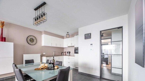 A modern kitchen with white cabinets, a glass dining table, and a built-in oven. - Cosy Apartment in Oostende With Private Terrace (Ostend)