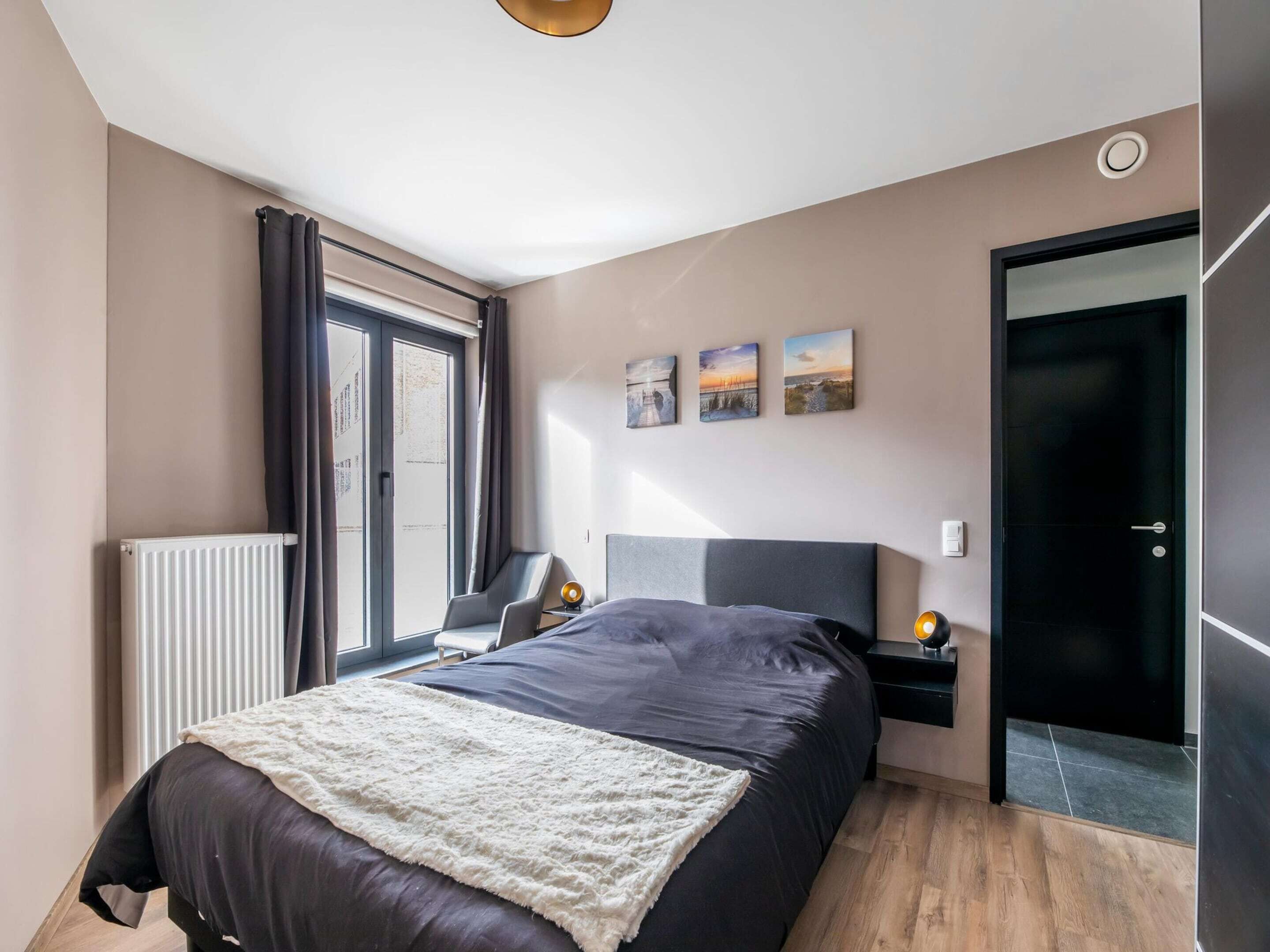 Un dormitorio moderno con una cama grande, un radiador, un escritorio y una puerta.