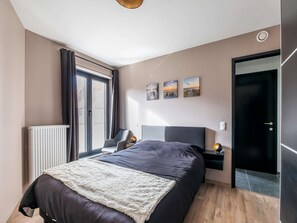 A modern bedroom with a large bed, a radiator, a desk, and a door. - Cosy Apartment in Oostende With Private Terrace (Ostend)