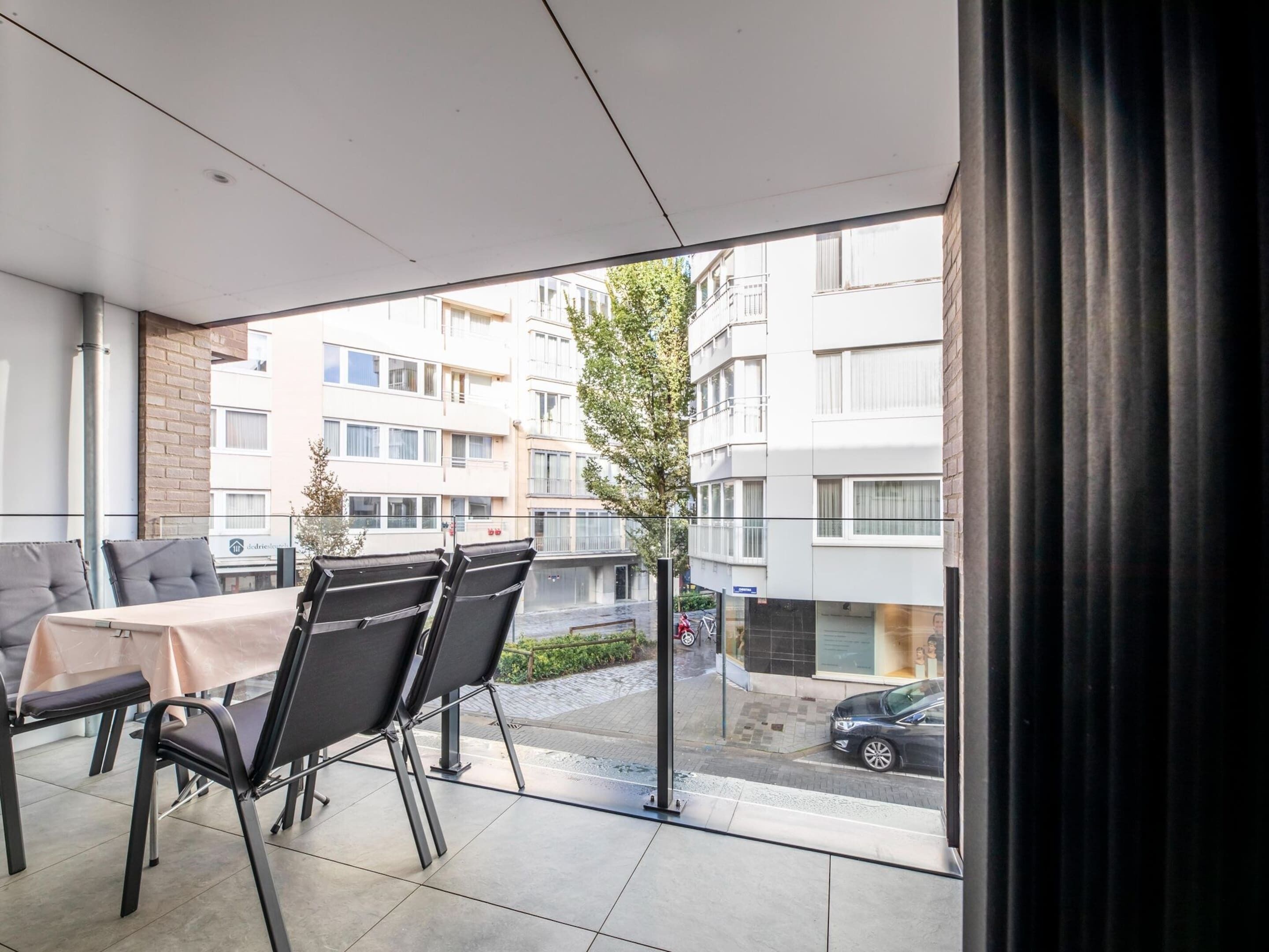 A modern apartment with a balcony, a dining area with a table and chairs, and a view of a residential building and street.