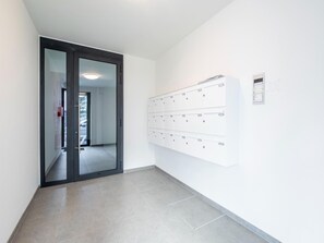 A hallway with a glass door leading to a parking area, a row of white lockers on the right, and a tiled floor. - Cosy Apartment in Oostende With Private Terrace (Ostend)