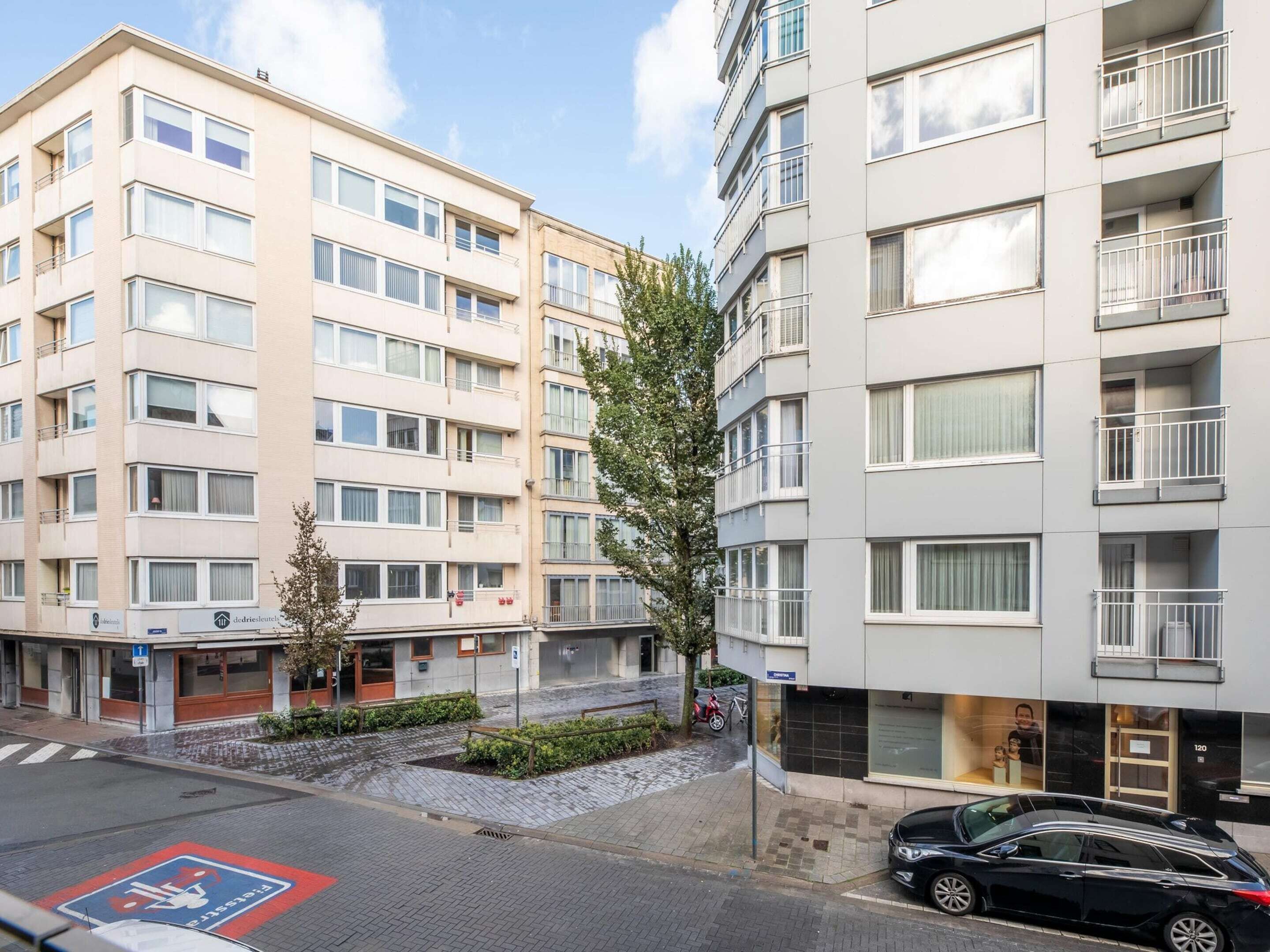 En flervåningsbyggnad med bostäder, balkonger, en parkeringsplats och en liten trädgård.
