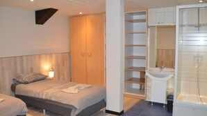 A bedroom with two beds, a wooden wardrobe, a built-in shelving unit, and a bathroom with a sink and bathtub. - Verviers Villa With Sauna (Verviers)