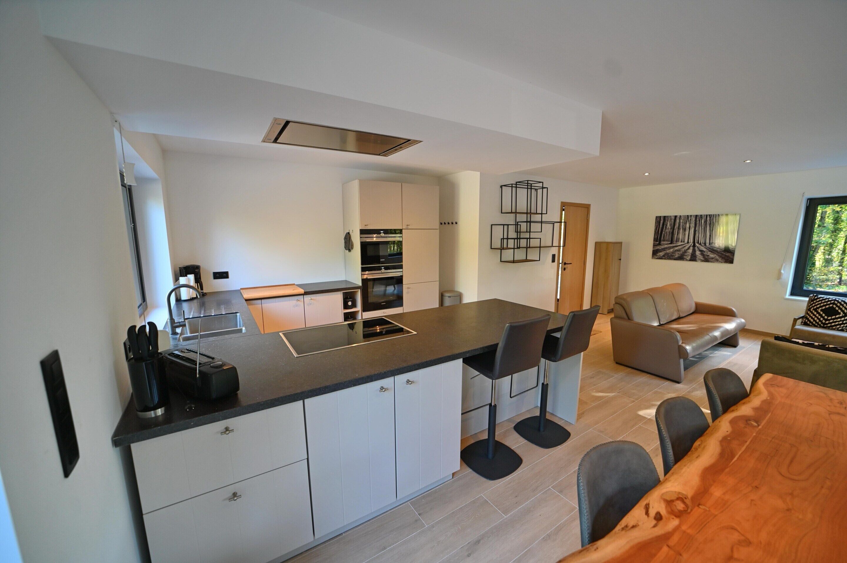 A modern kitchen with white cabinets, a black countertop, and a built-in oven. There is a dining area with a wooden table and chairs.