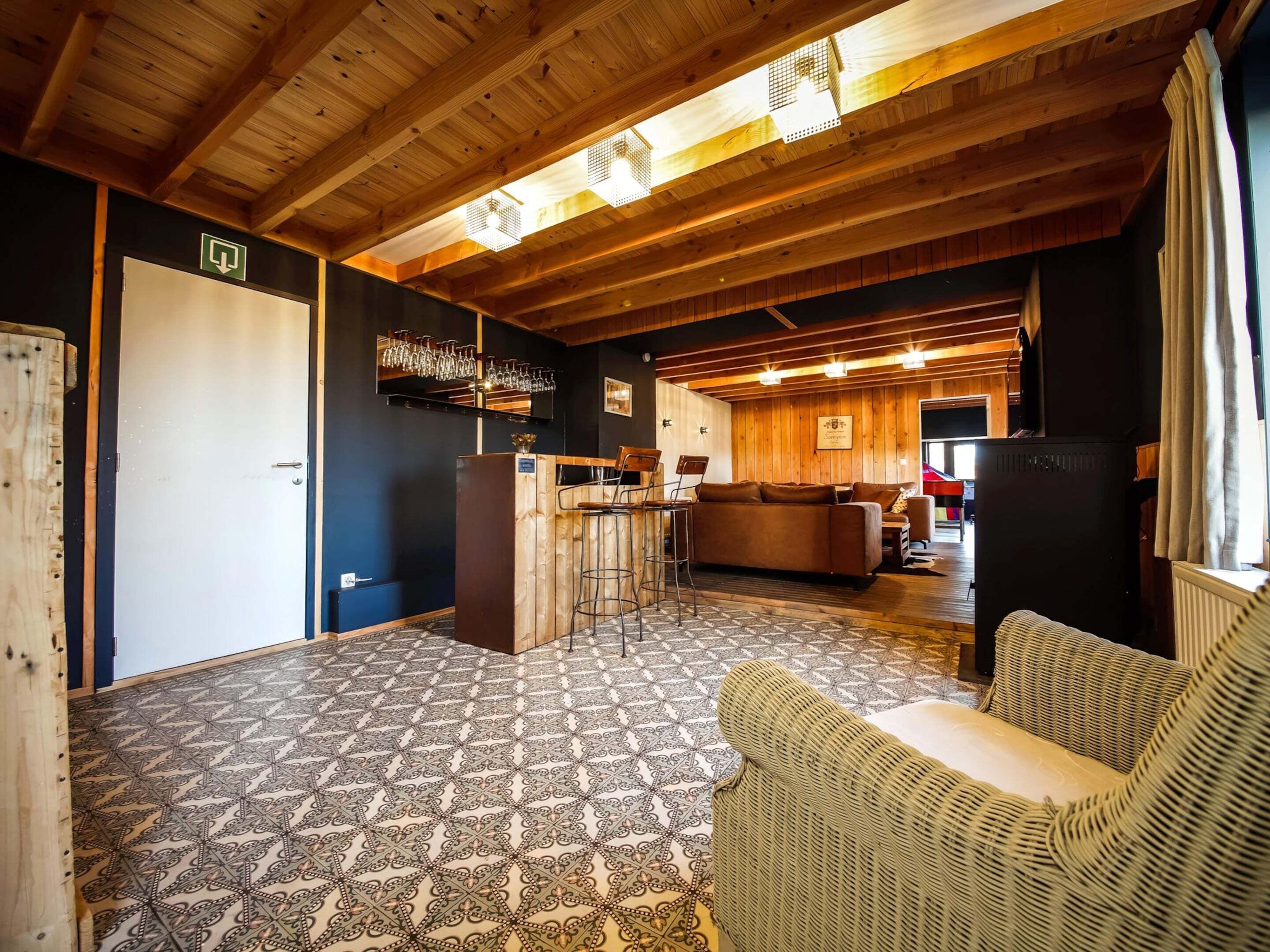 A cozy interior with a wooden ceiling, patterned floor, a bar area, and a seating area with a wicker sofa.