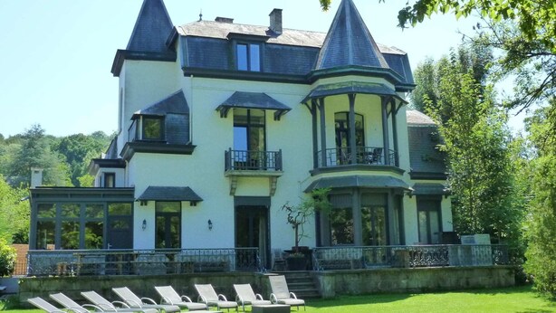A large, two-story building with a turret and balcony, surrounded by a well-maintained lawn and lounge chairs. - Modern Holiday Home in Hastiere With Sauna (Hastiere)
