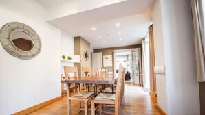 A dining area with a wooden table and chairs, a round mirror on the wall, and a kitchen in the background. - Modern Holiday Home in Hastiere With Sauna (Hastiere)