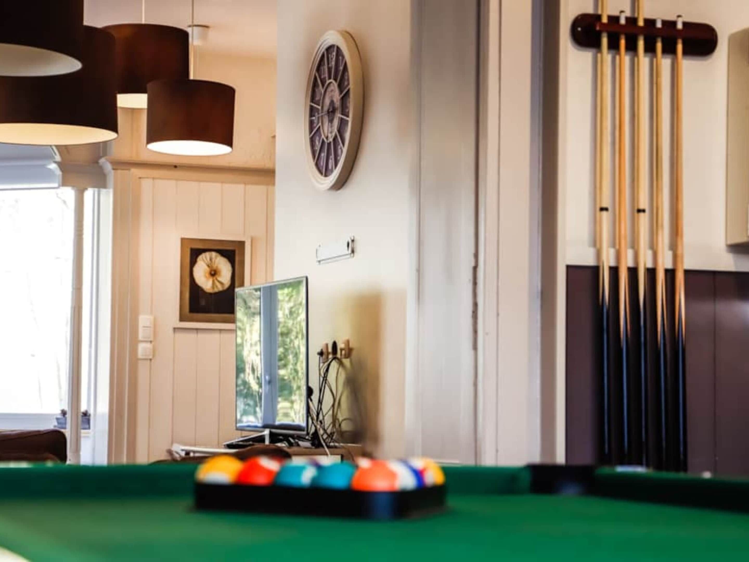 A billiards table with balls, a clock, and cue sticks on the wall.