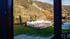 A view of a riverside area with a dock and a building with a fenced deck. - Modern Holiday Home in Hastiere With Sauna (Hastiere)