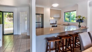 A modern kitchen with a large island, bar stools, and a view of greenery outside. - Sunset Waters 19 Hamilton Island - golf buggy and transfers (Hamilton Island)