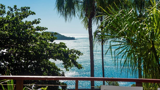 A view of a coastal area with a clear blue sea, palm trees, and a distant island. - Sunset Waters 19 Hamilton Island - golf buggy and transfers (Hamilton Island)