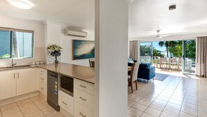 A modern kitchen with a dishwasher, a dining area with a blue sofa and a table, and a balcony with a view of the outdoors. - Sunset Waters 19 Hamilton Island - golf buggy and transfers (Hamilton Island)