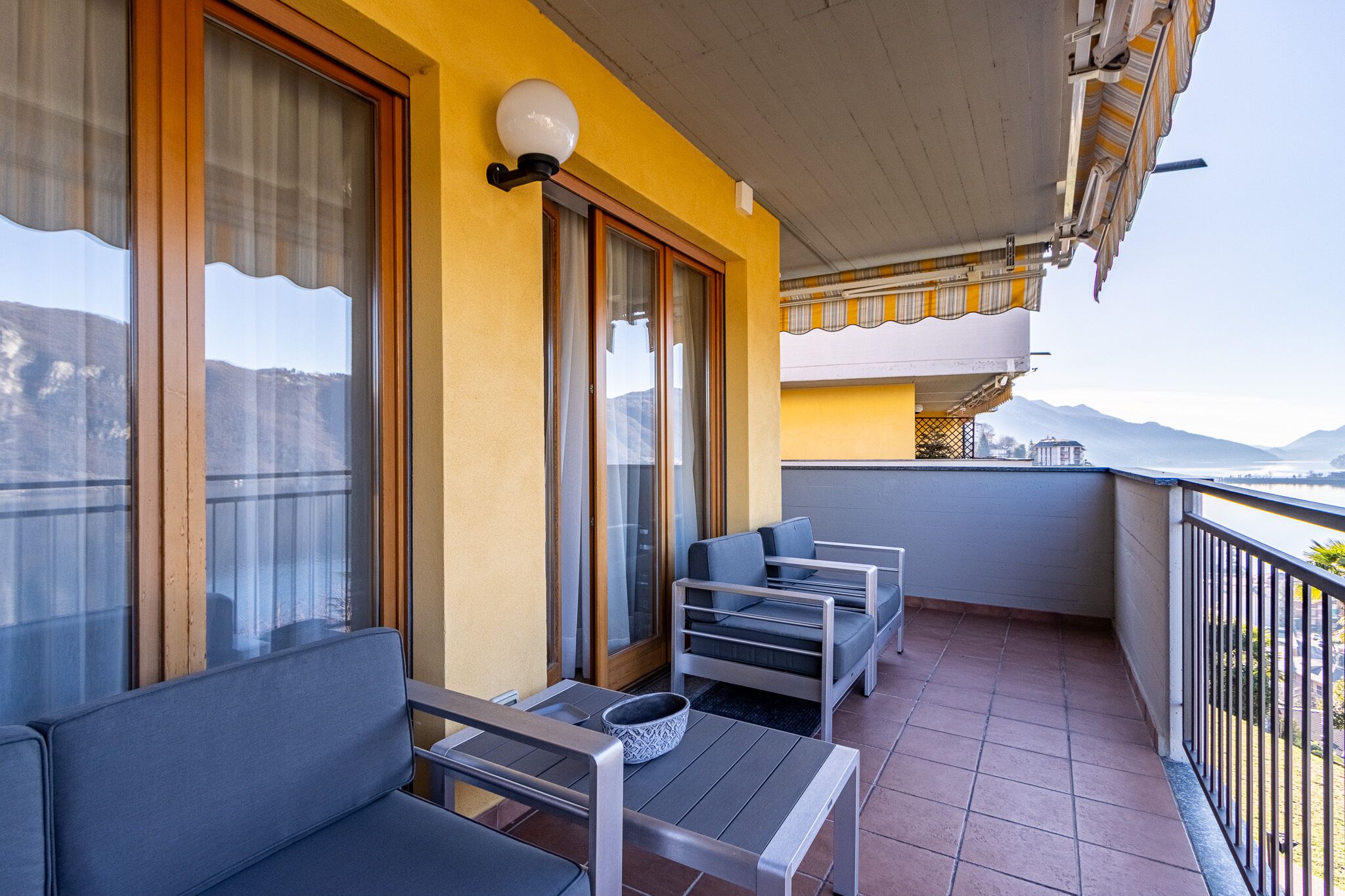 A balcony with a sofa, a table, and a chair, overlooking a scenic view.