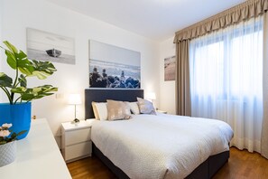 A neatly arranged bedroom with a large bed, bedside tables, a nightstand, and a potted plant.