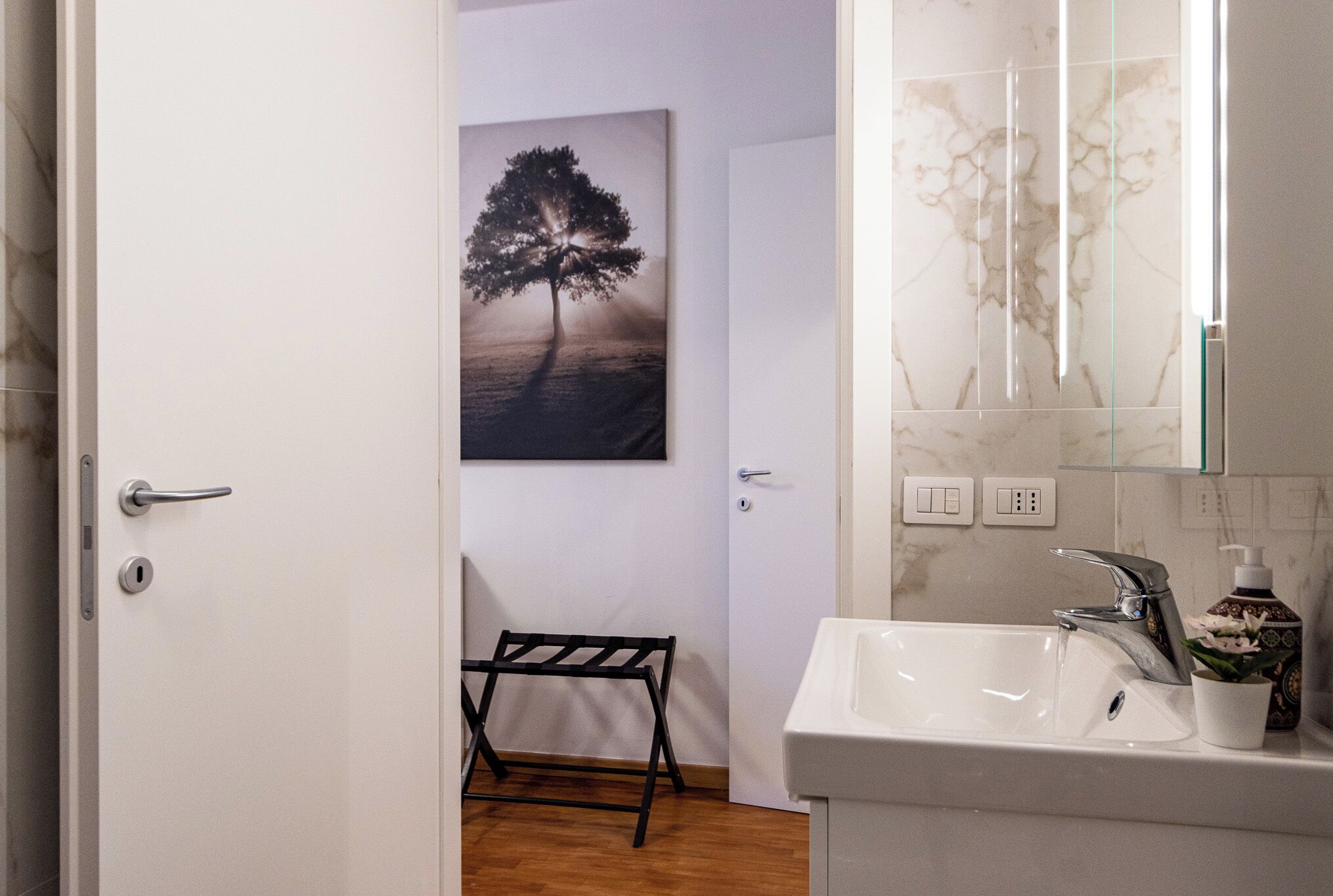 Ein Badezimmer mit einem weißen Waschbecken, einem Spiegel und einem Baumgemälde an der Wand.