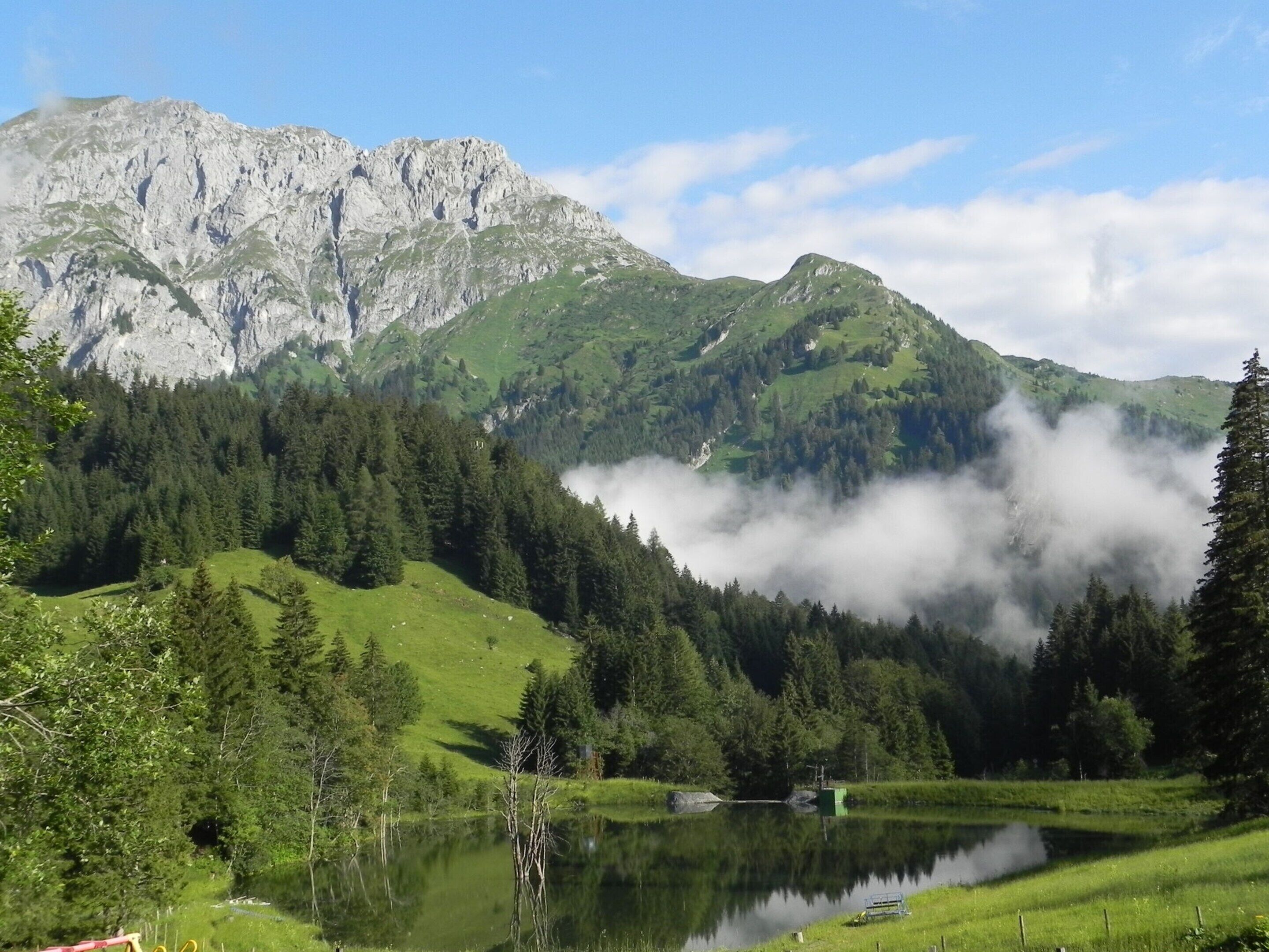 A mountainous landscape with a lake, forested hills, and a clear sky.