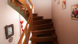 Μια ξύλινη σκάλα με ένα στηρίγμα για το χέρι, που οδηγεί σε έναν ανώτερο όροφο. Οι τοίχοι είναι διακοσμημένοι με φωτογραφίες σε κορνίζες και ένα διακοσμητικό στοιχείο σε σχήμα καρδιάς.