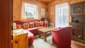 Interior acogedor de una cabaña con techo de madera, un sofá rojo con cojines estampados, una mesa de madera y un sillón rojo.