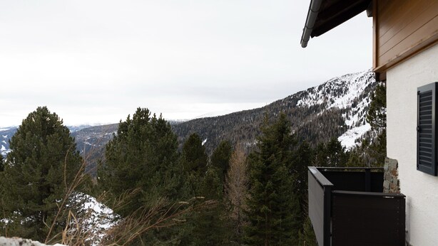 Una cabaña en la montaña con vistas a laderas nevadas y un bosque denso.