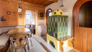 Interior rústico de madera con una mesa de comedor, sillas, un sofá y una estufa verde en forma de queso.