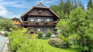 A traditional wooden chalet with a balcony adorned with flowers, surrounded by lush greenery and a mountainous backdrop. - Holiday Home in Bad Kleinkirchheim (Bad Kleinkirchheim)