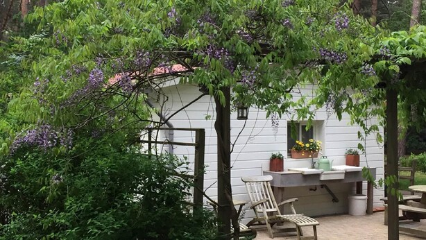 A rustic outdoor seating area with a wooden table and chairs, surrounded by lush greenery and purple flowers. - Gierle Garden Bungalow Escape (Lille)