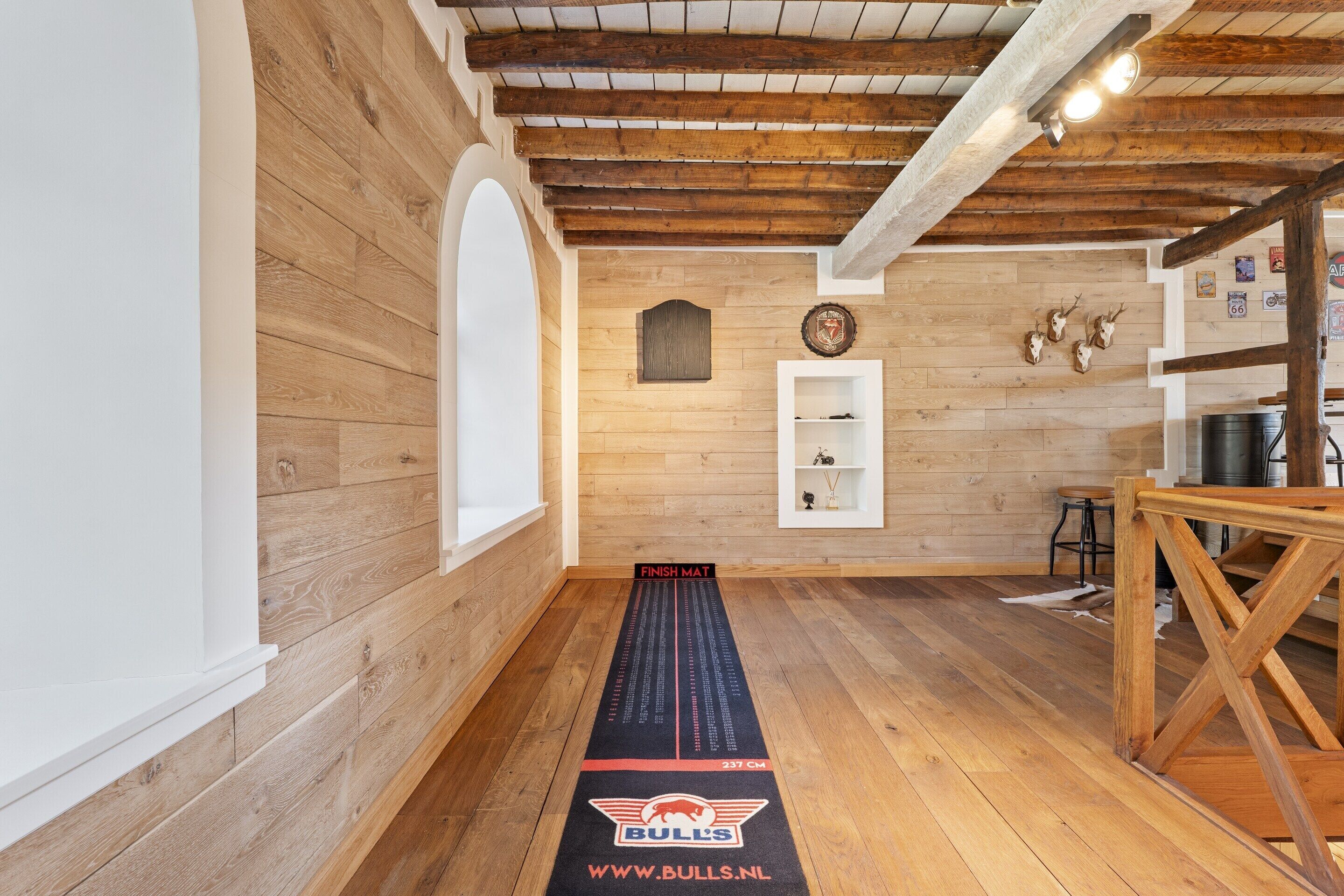 A room with wooden walls and a wooden ceiling, a white shelf with decorative items, and a mat with text and logos.