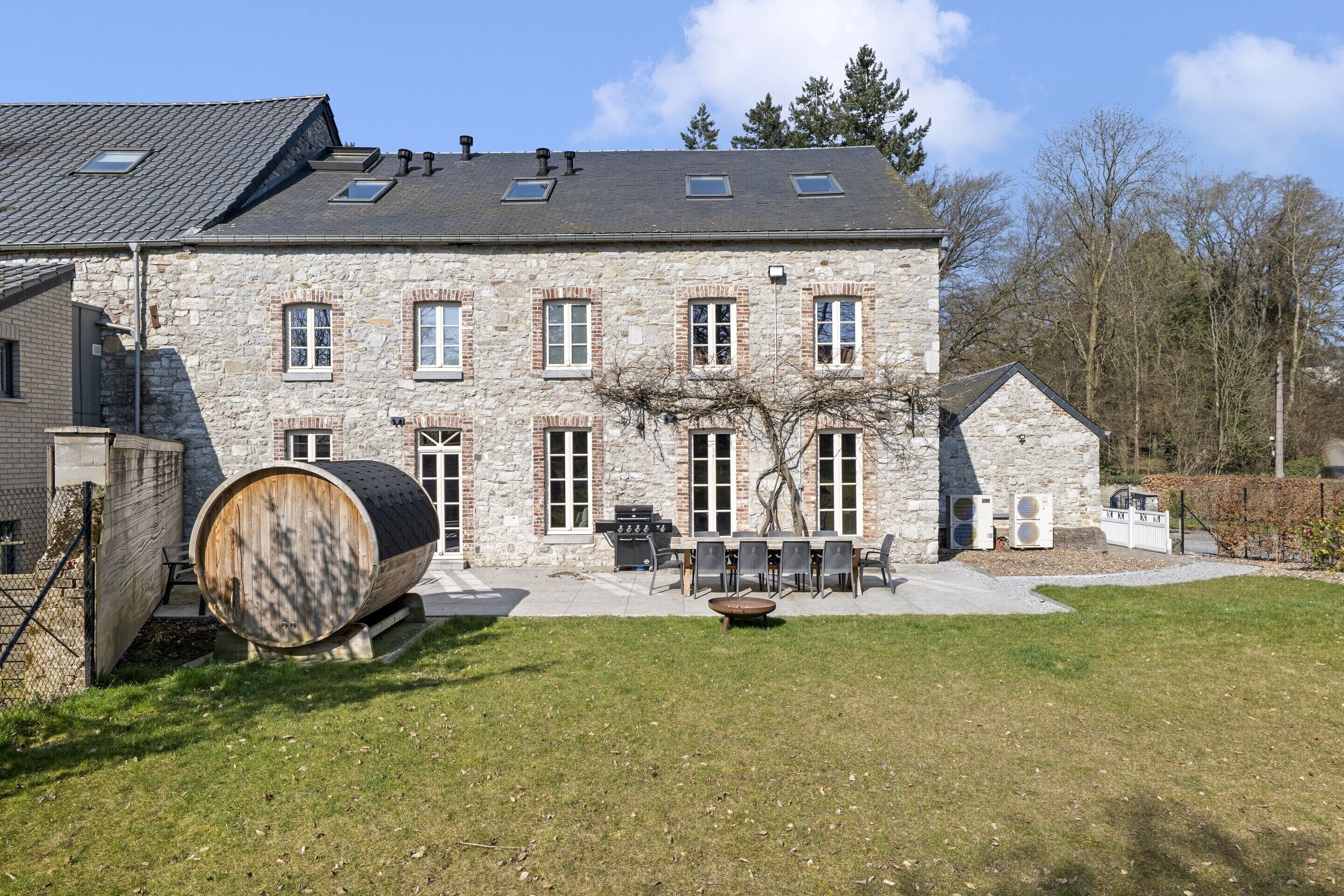 A stone building with a large barrel, outdoor seating, and a well-maintained lawn.