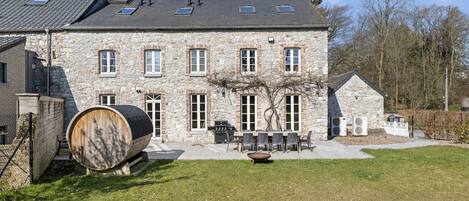 A stone building with a large barrel, outdoor seating, and a well-maintained lawn.