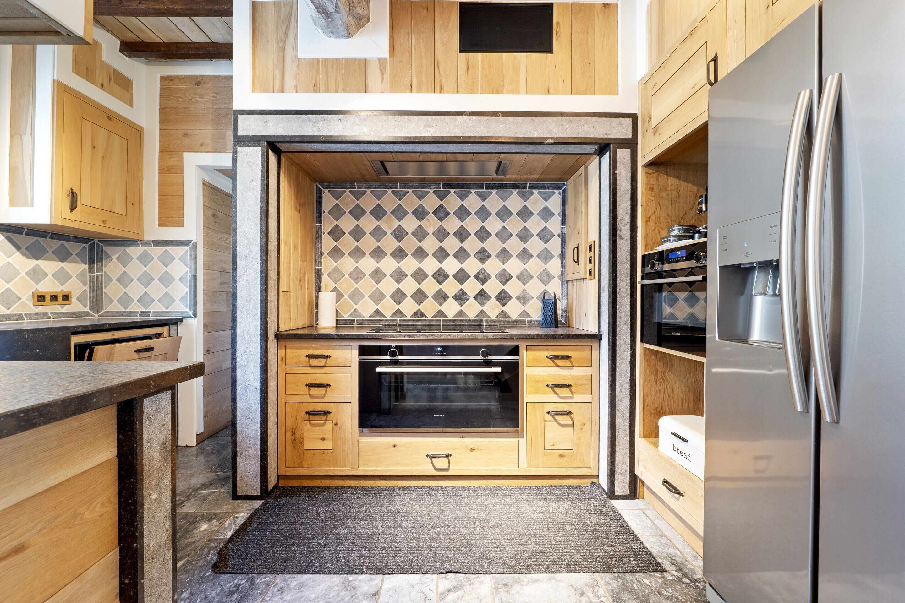 A modern kitchen with wooden cabinetry, a built-in oven, and a stainless steel refrigerator.