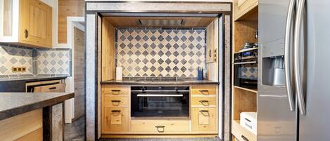 A modern kitchen with wooden cabinetry, a built-in oven, and a stainless steel refrigerator.