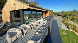 Un área de estar moderna al aire libre con estructura de madera, paredes de vidrio y vistas al paisaje.
