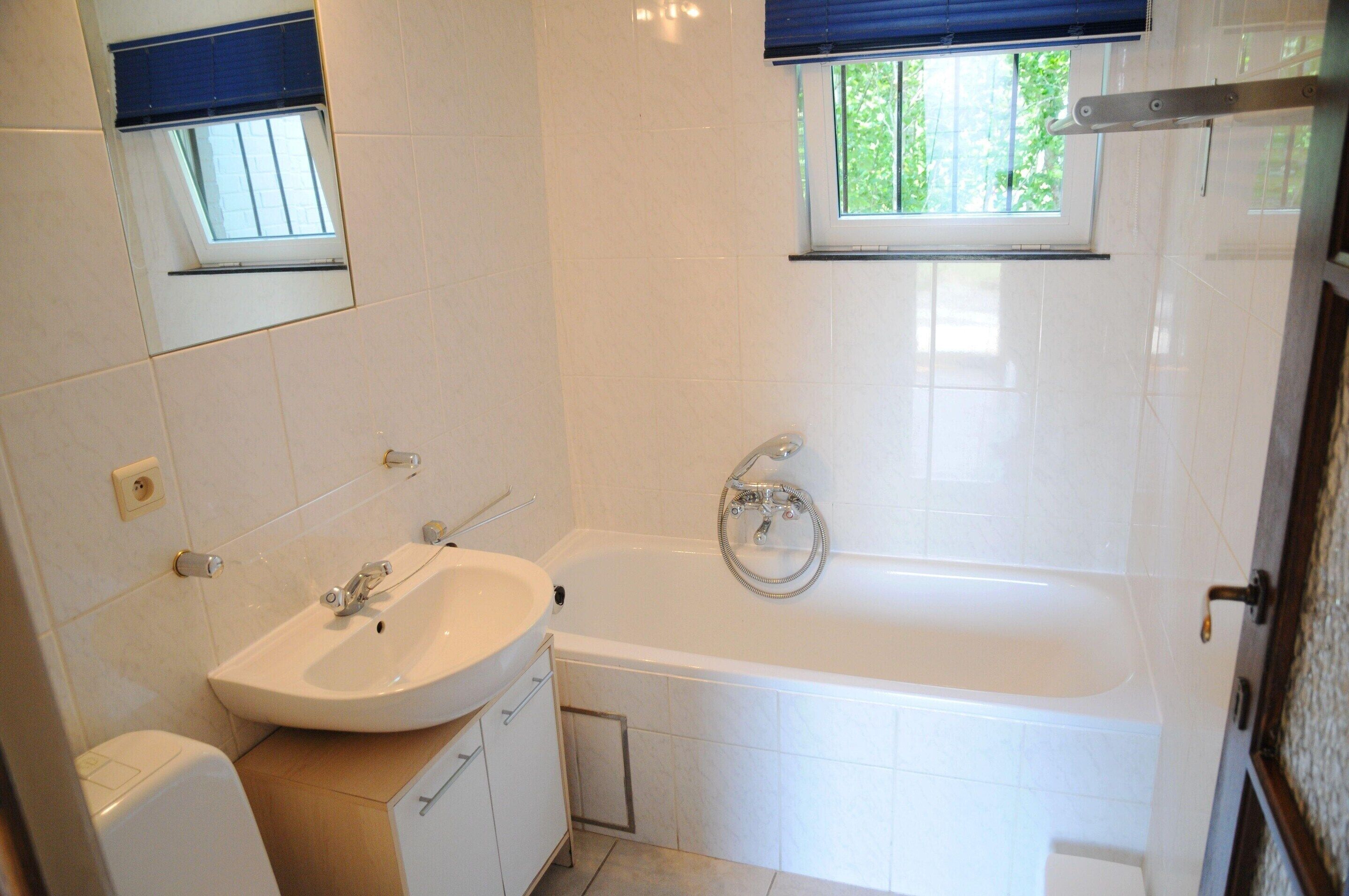 A bathroom with a sink, mirror, window, and bathtub.