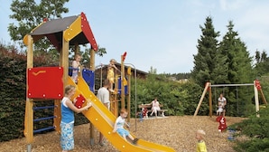 Ein Spielplatz mit Rutsche, Klettergerüsten und einem überdachten Spielbereich.