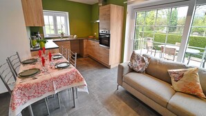 A modern kitchen with wooden cabinets, a dining table set with plates and cutlery, and a sofa with floral cushions.