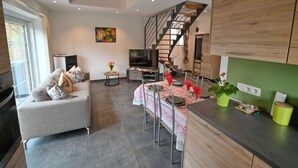 A modern kitchen with a dining area, a staircase, and a living room with a sofa and a TV.