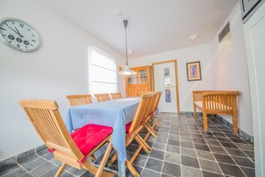 A dining area with a table set for six, wooden chairs, a checkered tablecloth, and a red cushion on one chair. A wall clock is visible, and there is a door leading to another room. - Holiday Home With a Terrace in Warisy (Rendeux)