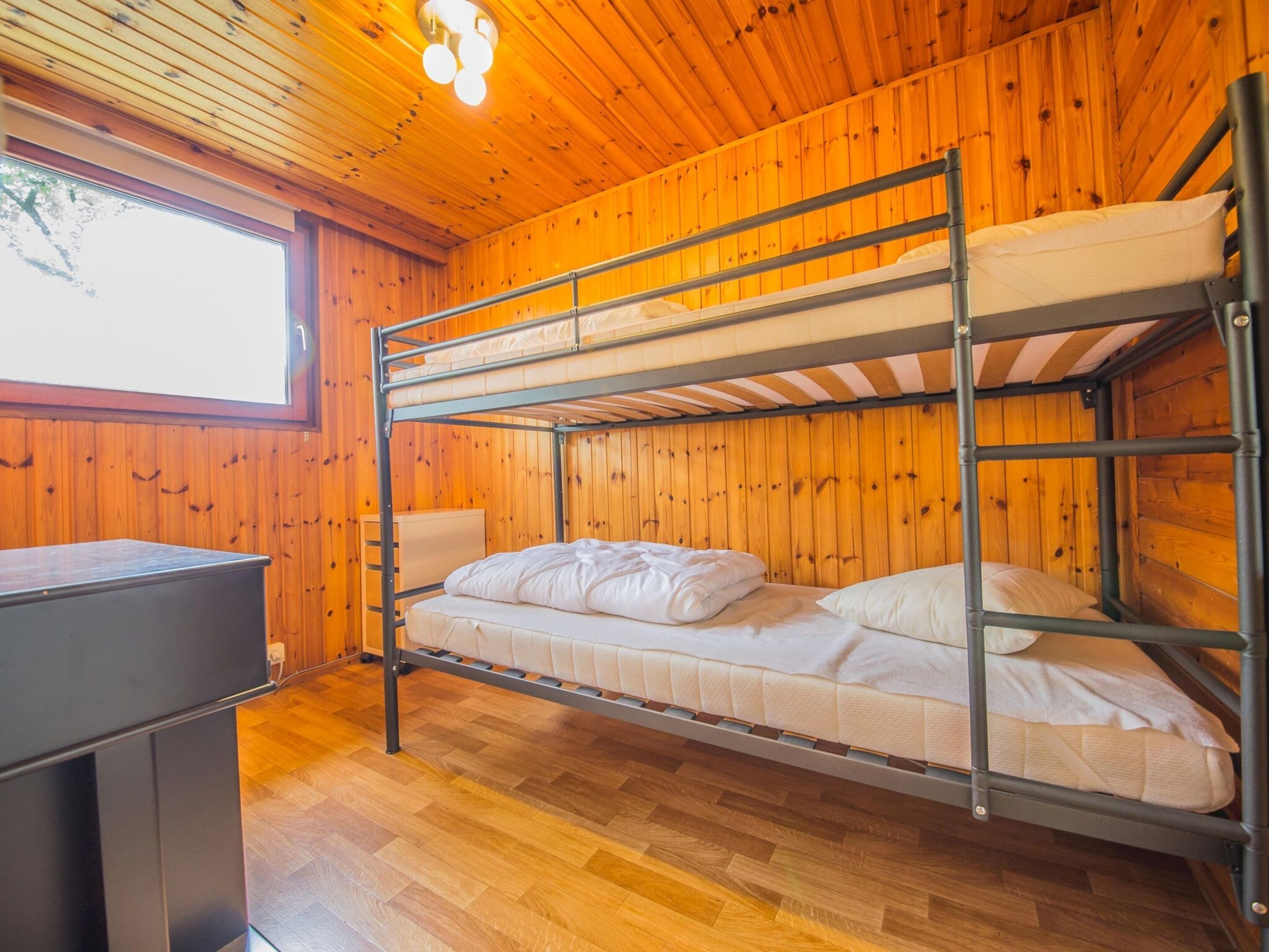 Une chambre avec un lit superposé, des murs en bois et une fenêtre.