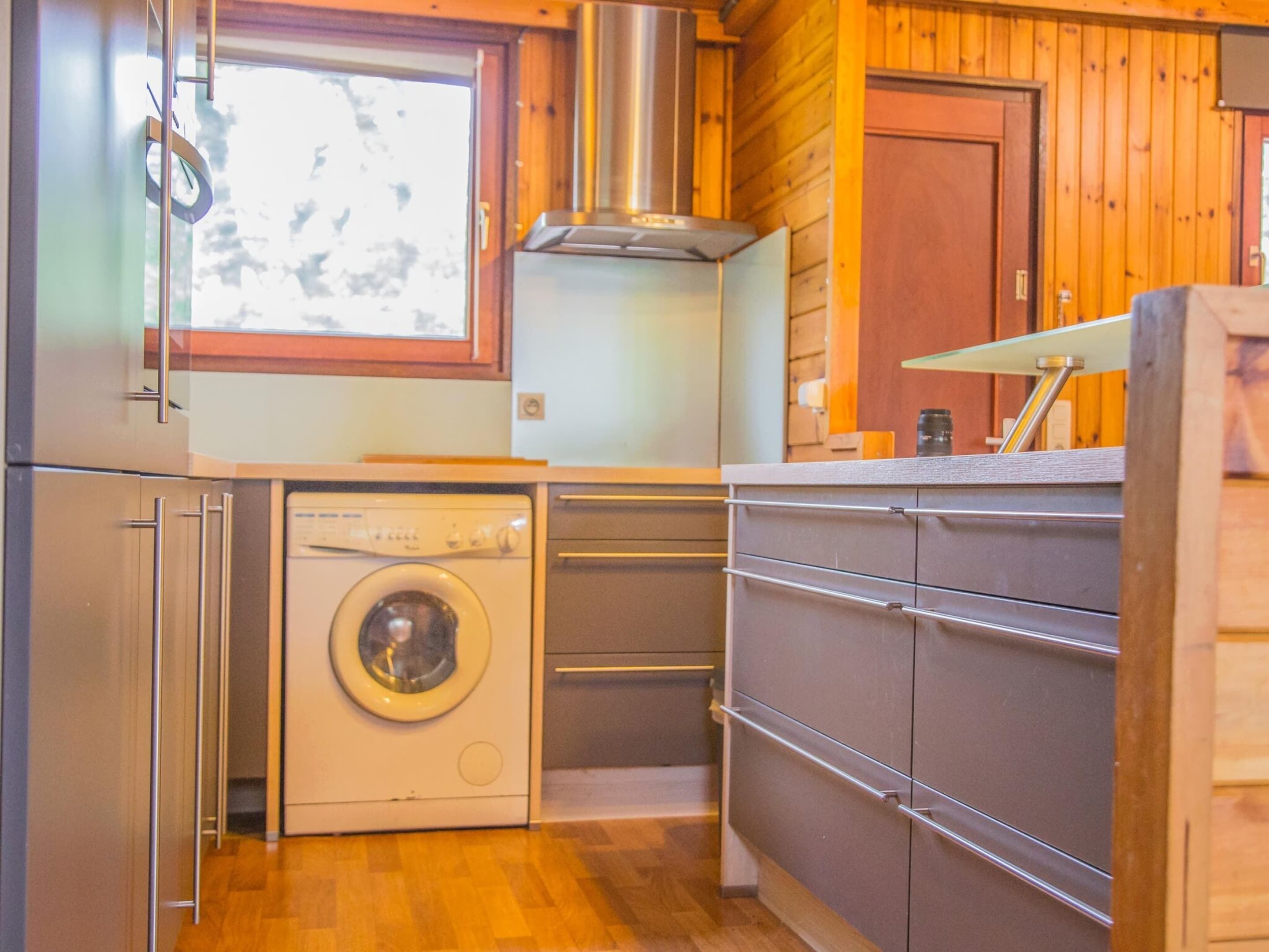 A compact kitchen with a washing machine, wooden cabinets, and a window.