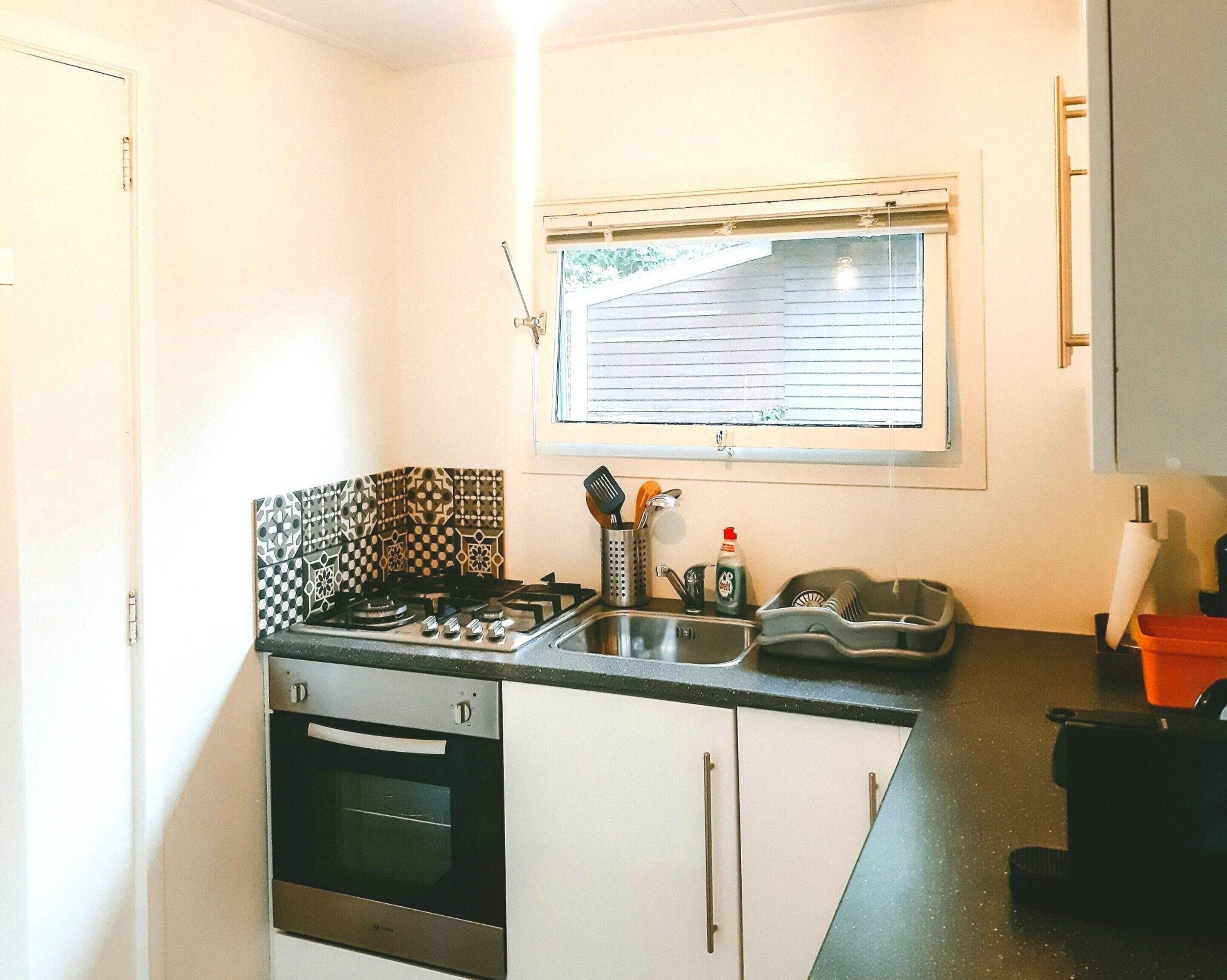 Una cocina compacta con estufa a gas, horno y una ventana con persianas.