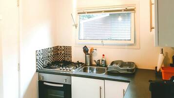 Una cocina compacta con estufa a gas, horno y una ventana con persianas.