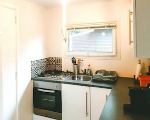 A compact kitchen with a gas stove, oven, and a window with blinds. - Beautiful Romantic Chalet in Geel (Geel)
