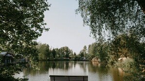 Puinen penkki rauhallisen järven rannalla, taustalla näkyy taloja.