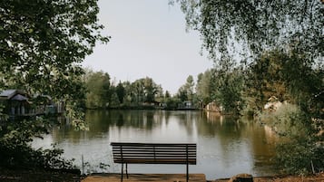 A wooden bench by a calm lake with houses in the background.
