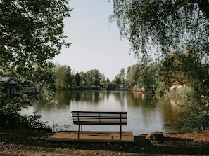 En træbænk ved en rolig sø med huse i baggrunden.