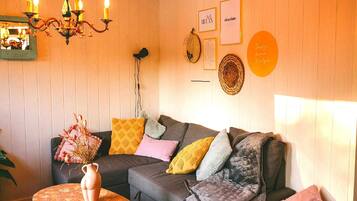 A cozy living room with a sofa, cushions, a table with a vase, a chandelier, and wall decorations.