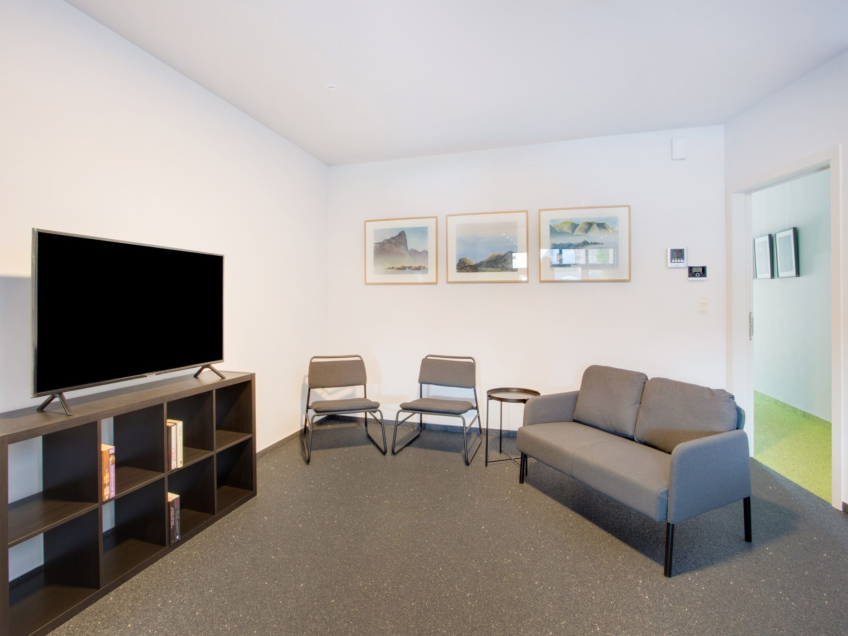 A modern living room with a flat-screen TV, two chairs, a sofa, and a bookshelf.